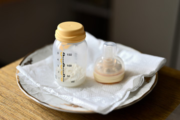 Bottle with dried milk and pacifier in plastic cover on plate.