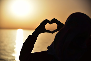 A young muslim woman making heart symbol with her hands at sunset.