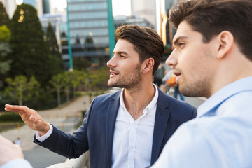 Handsome unshaved two friends colleagues business men outdoors on the street talking with each other.