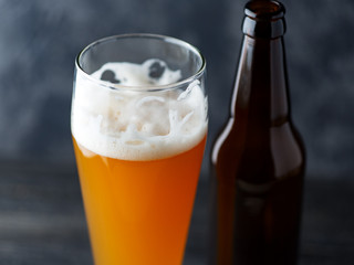 Close-up of a glass of cold unfiltered wheat beer and a beer bottle on a dark background