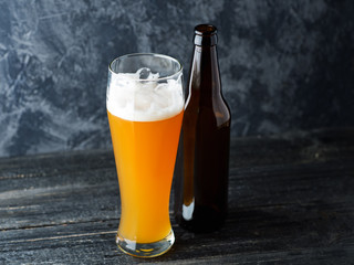 Close-up of a glass of cold unfiltered wheat beer and a beer bottle on a dark background
