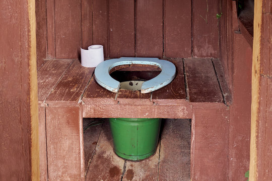 Interior of a country wooden outdoor toilet with a metal bucket as a waste tank and a roll of a paper