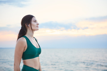 Young brunette woman exercising at the sea shore at sunrise listening to the music.