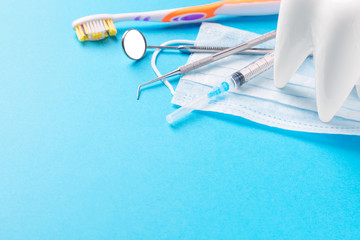 Dental hygiene and health concept. Dentist tools or instruments dental explorer, probe, dental mirror, syringe, white tooth model, toothbrush and face mask on light blue background.