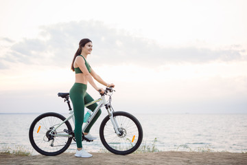 Fototapeta premium Young brunette woman on a bicycle at sunrise.