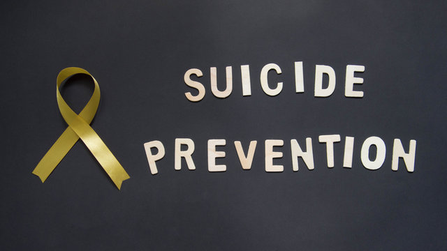 World suicide prevention day, 10th September. Yellow ribbon awareness and SUICIDE PREVENTION wooden word on black background. Mental health care concept.