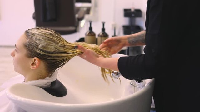 close up blondie girl in a beauty salon applying balsam on hair tattoos hands