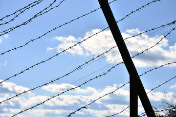 Black silhouette of old barb wire fence on blue sky. Symbol of lack of freedom, poverty, limitations, old times, communist regime, iron curtain