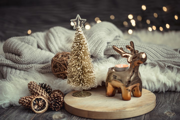 Christmas festive background with toy deer with a gift box and Christmas tree, blurred background with golden lights on wooden deck table