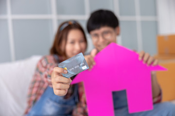 selective focus and close up credit card on hand with paper house and young couple asian background