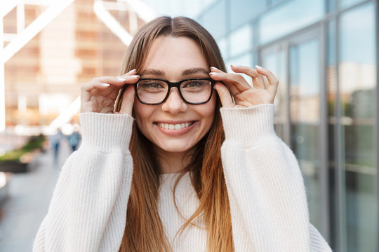 Beautiful young happy excited business woman posing walking outdoors near business center wearing eyeglasses.