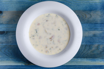cheese soup with vegetables in a white plate on a blue background 
