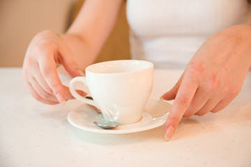 Holds cup with drink in his hands on table