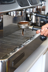 Fototapeta na wymiar Waitress holding a professional coffee portafilter to make a perfect espresso for a a creamy cafe latte. Workplace illustrative of a cafeteria coffee shop. Brown crushed beans powder.