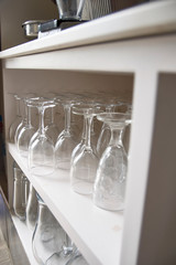 Sorted organized wine glass cups in a restaurant shelving shelf. Bottom view. Shiny and clean light. White, elegant modern interiors of bar.