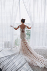 the bride in the dress stands at the large panoramic window