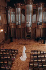 the bride in a dress with a long veil is in a large beautiful organ hall