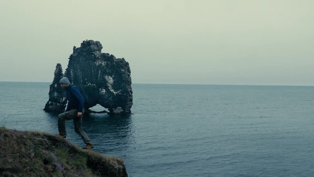 A man looking at the view, then he goes up out of the frame. Sea and rocks in the background.