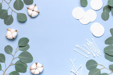 Cotton Cosmetic Makeup Removers Tampons. Spa concept. Flat lay background with cotton flowers, cotton pads, eared sticks, fresh eucalyptus twigs. Hygienic sanitary swabs on blue background Top view