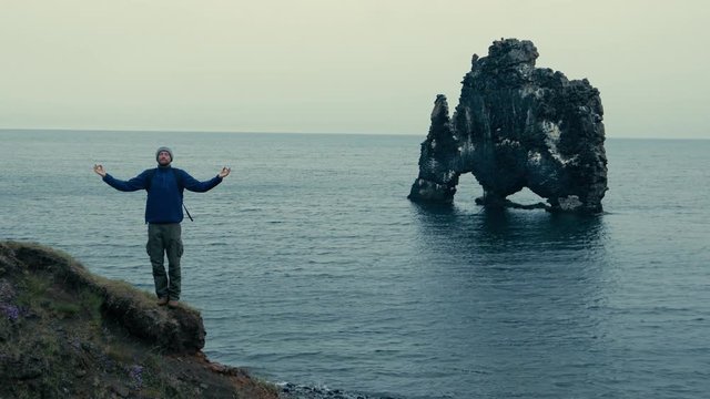 Man meditating on the rocks in Iceland. His arms are apart. He is standing. Sea in the background.