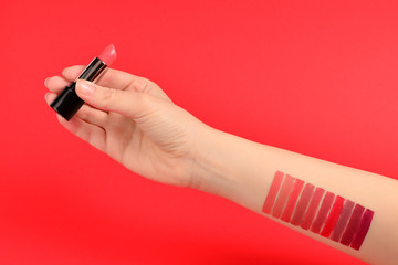 Lipstick swatches on woman hand isolated on red background.