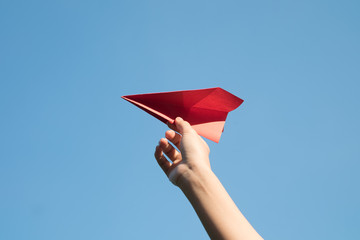 Woman hand holding a red paper rocket with a bright blue background.