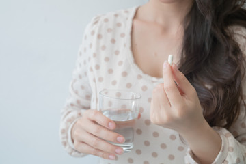 A woman holding a medicine and a glass of water in her hand. Medical and health concepts