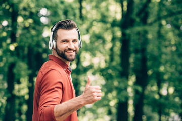 young man listening to music on headphones and showing thumb up