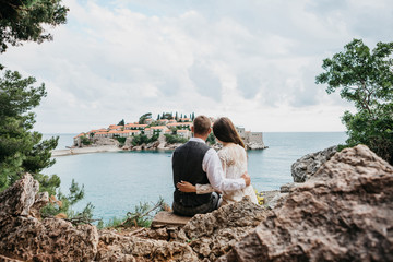 Fototapeta premium A man and a woman admire a beautiful view of the island of Sveti Stefan in Montenegro. He hugs her.