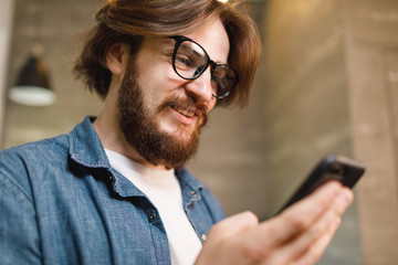 Obraz na płótnie Canvas Bearded man wearing glasses smiling while holding smartphone