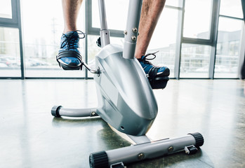 cropped view of sportsman training on elliptical machine at gym
