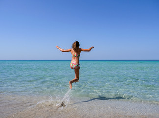 Slim and athletic girl in a colourful bikini jumping into the crystal clear water of a beautiful beach -vacation-fitness-wellness
