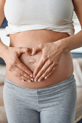 Young pregnant woman making a heart gesture with her hands around her bare belly button signalling her love for her unborn child