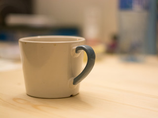 White and blue unwashed cup of coffee on a flat wooden surface in front of bokeh office desk background
