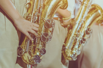 Male student with friends blow the saxophone with the band for performance on stage at night.