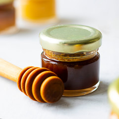 Small glass jar close up of dark brown honey with kerob syrup with metal cap and special wooden spoon isolate on grey cement background with copy space. Healthy product natural, Square Selective focus