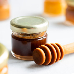 Small glass jar close up of dark brown honey with kerob syrup with metal cap and special wooden spoon isolate on grey cement background with copy space. Healthy product natural, Square Selective focus
