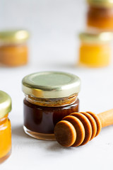 Small glass jar close up of dark brown honey with kerob syrup with metal cap and special wooden spoon isolate on grey cement background, copy space. Healthy product natural, Vertical Selective focus