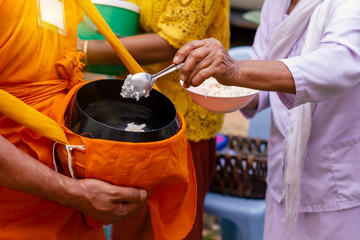 Thai people put food to a monk's alms bowl in the end of Buddhist Lent Day