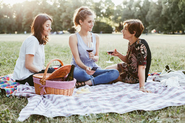 Mother and two daughters make picnic in a park at sunset during summer