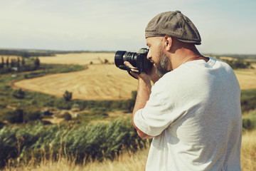 Obraz premium photographer with a camera stands on the background of cereal fields. a man wearing shorts and a t-shirt, a cap on his head