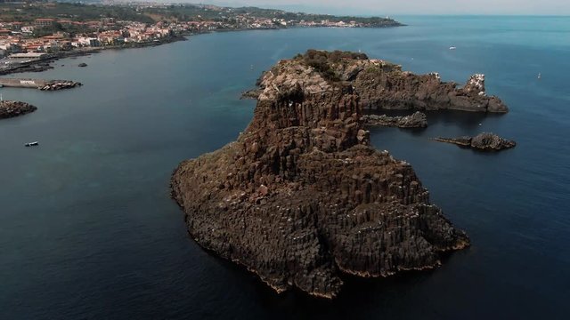 Aerial orbiting view of the faraglioni and the fishing village of Aci Trezza on the East coast of Sicily