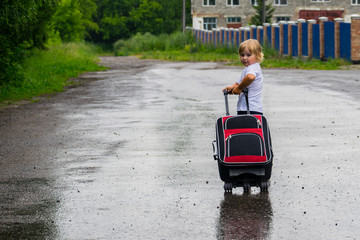 Lonely little girl walking in the rain on the road with a suitcase.