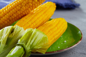 Two ears of boiled corn with leaves on a plate in the kitchen.