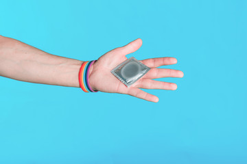 Hand with LGBT bracelet holding a condom. The concept of safe sex life for gay lesbian and transgender people