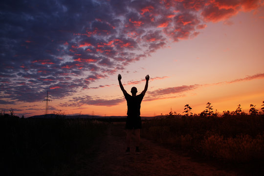 dark silhouette of a man raised his hands up towards the sky with a beautiful pink sunset with purple clouds