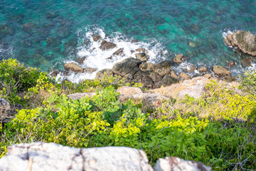 Looking over a cliff edge with blue sea below and Cliff edge and the sea. Stones worn smooth along the top of a cliff and a blue sea below.