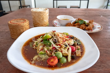 green papaya salad in White plate and sticky rice on wooden background.