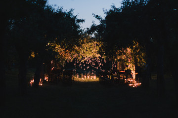 Coziness and style. Modern event design. Lounge zone and european traditional wedding ceremony decoration outdoors in the evening, decorated with candles and lights.