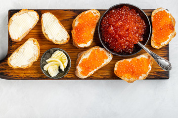Close-up red caviar in bowl and Sandwiches on wooden cutting board on white background. Top view with copy space. Flat lay